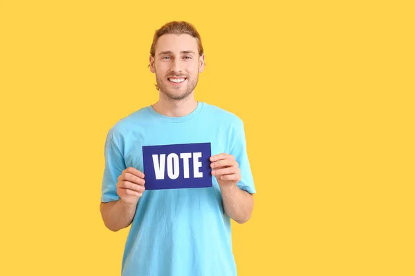 Young man holding paper with text VOTE on color background — Stock Photo, Image