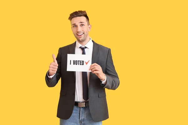 Biznesmen trzymający papier z tekstem Głosowałem i pokazujący kciuk do góry na tle koloru — Zdjęcie stockowe