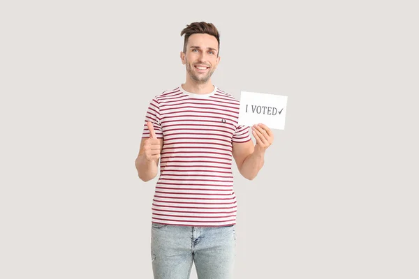 Young man holding paper with text I VOTED and showing thumb-up on light background — Stock Photo, Image