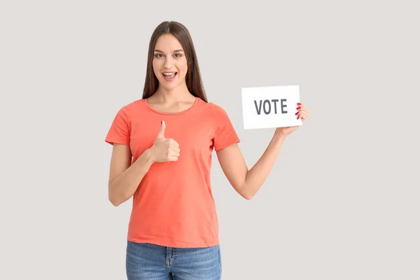 Jovem segurando papel com texto VOTE e mostrando polegar para cima no fundo claro — Fotografia de Stock