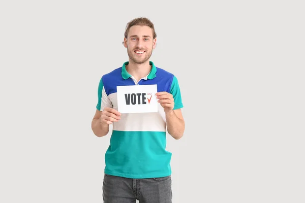 Young man holding paper with text VOTE on light background — Stock Photo, Image
