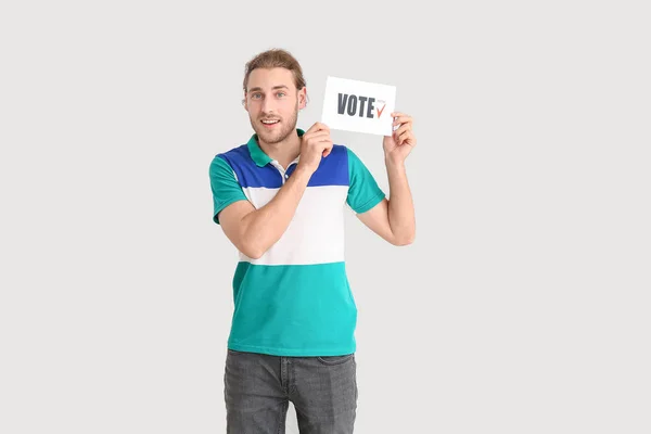 Young man holding paper with text VOTE on light background — Stock Photo, Image