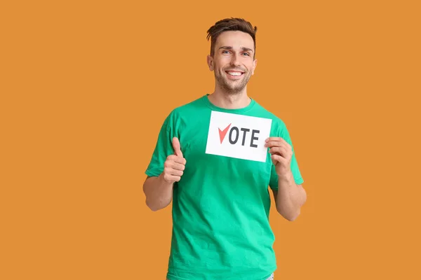 Jovem segurando papel com texto VOTE e mostrando polegar para cima no fundo de cor — Fotografia de Stock