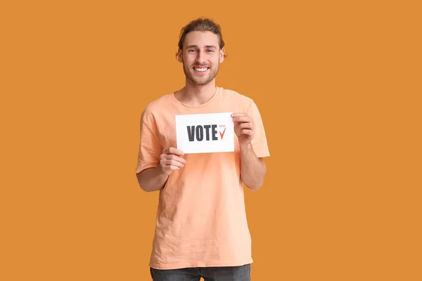 Young man holding paper with text VOTE on color background — Stock Photo, Image