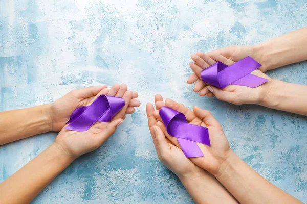 Женские руки с фиолетовыми лентами как символ Всемирного дня борьбы с раком на цветном фоне — стоковое фото