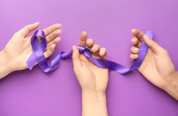 Kvinnliga händer med lila band som symbol för World Cancer Day på färg bakgrund — Stockfoto