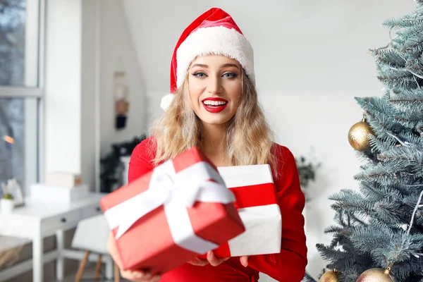 Noel Baba şapkalı güzel bir kadın Noel ağacının yanında hediyeler getirmiş. — Stok fotoğraf
