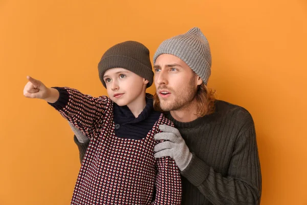 Man and his little son in winter clothes on color background — Stock Photo, Image