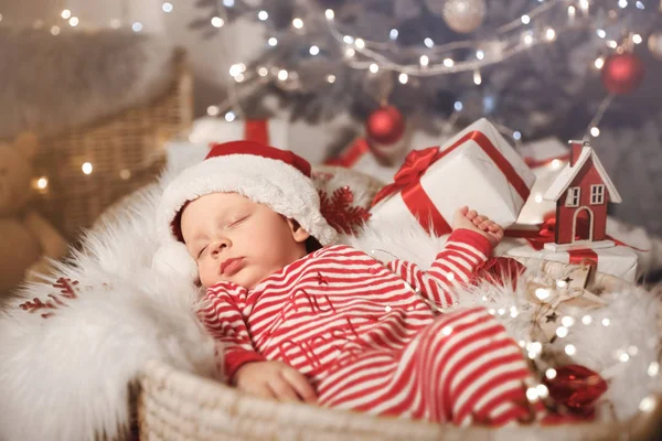 Bebê bonito com chapéu de Papai Noel e presente de Natal dormindo em cesta em casa — Fotografia de Stock