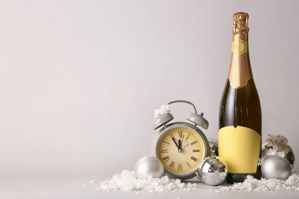 Butelka szampana, świąteczny wystrój i budzik na jasnym tle — Zdjęcie stockowe