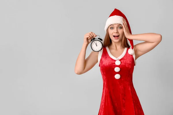 Surprise jeune femme en costume de Père Noël et avec réveil sur fond clair. Concept de compte à rebours de Noël — Photo