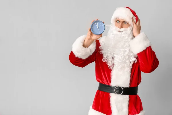 Confused Santa Claus with alarm clock on light background. Christmas countdown concept — Stock Photo, Image