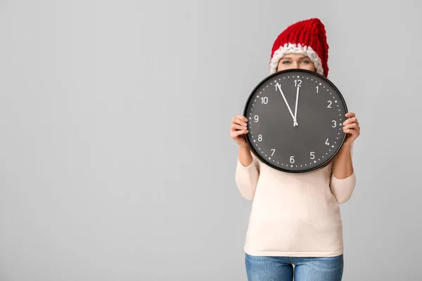 Jovem mulher em chapéu de Papai Noel e com relógio no fundo claro. Conceito de contagem regressiva de Natal — Fotografia de Stock