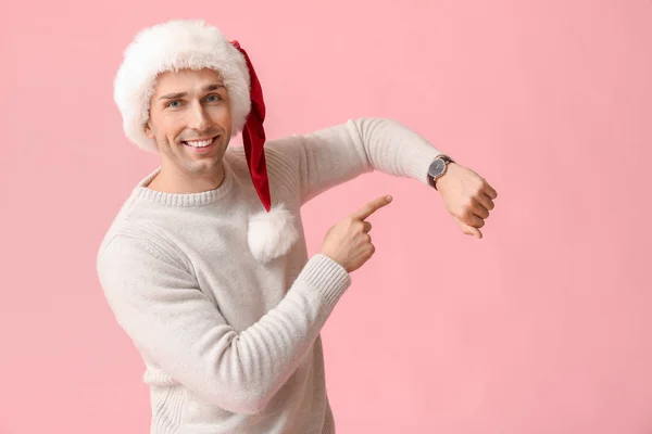 Young man in Santa hat and with watch on color background. Christmas countdown concept — Stock Photo, Image