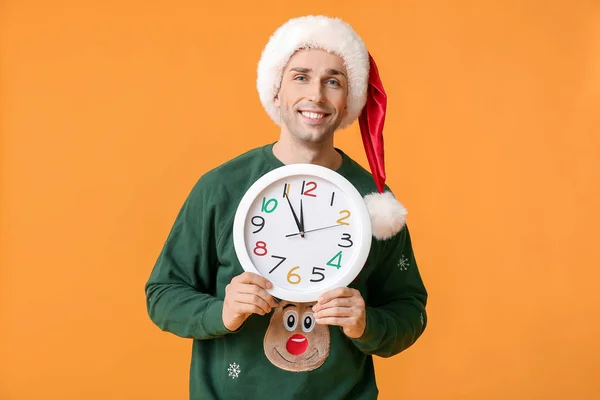 Young man in Santa hat and with clock on color background. Christmas countdown concept — Stock Photo, Image