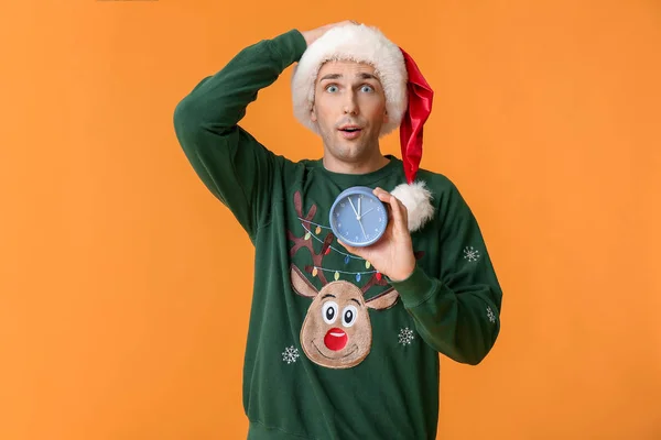 Surprised young man in Santa hat and with alarm clock on color background. Christmas countdown concept — Stock Photo, Image