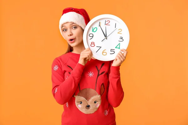 Giovane donna in cappello Babbo Natale e con orologio su sfondo a colori. Conto alla rovescia di Natale — Foto Stock