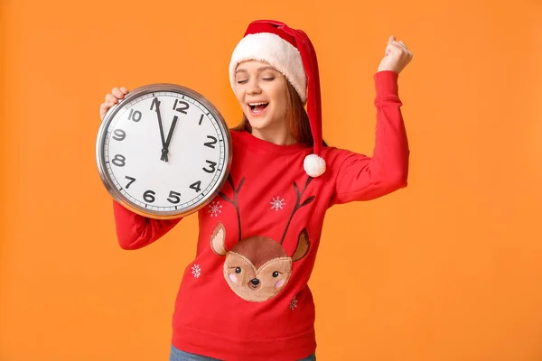 Giovane donna felice in cappello di Babbo Natale e con orologio su sfondo a colori. Conto alla rovescia di Natale — Foto Stock