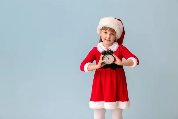 Dziewczynka w stroju Mikołaja i z budzikiem na tle koloru. Koncepcja odliczania świąt — Zdjęcie stockowe