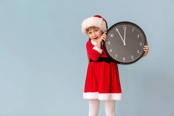 Liten flicka i Santa kostym och med klocka på färg bakgrund. Julnedräkning koncept — Stockfoto