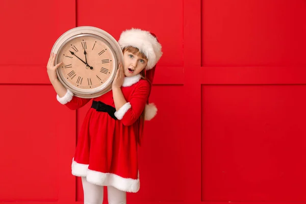 Liten flicka i Santa kostym och med klocka på färg bakgrund. Julnedräkning koncept — Stockfoto