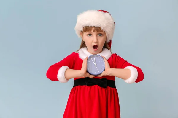 Menina surpreendida no traje de Santa e com despertador no fundo de cor. Conceito de contagem regressiva de Natal — Fotografia de Stock