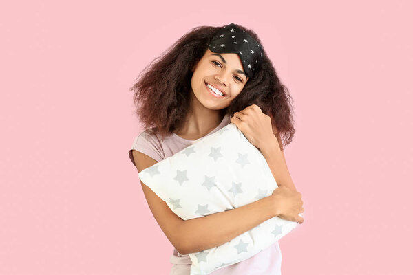 Beautiful African-American woman with sleep mask and pillow on color background