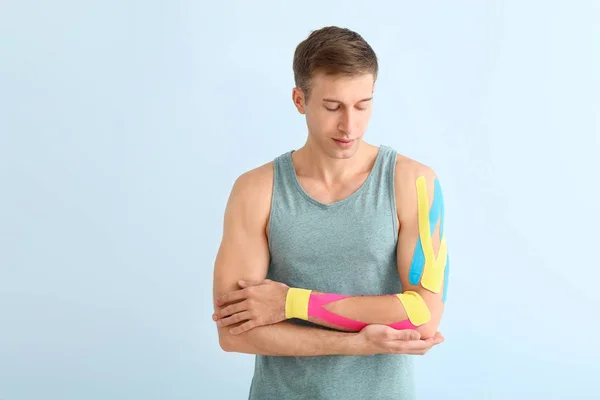 Uomo sportivo con nastro fisioterapico applicato sul braccio su sfondo chiaro — Foto Stock