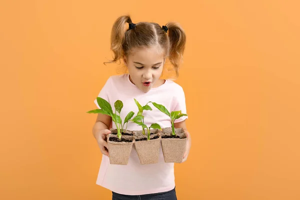 Surprised little girl with young plants in pots on color background — Stock Photo, Image