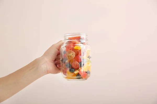 Female hand with tasty fruit salad in jar on light background — Stock Photo, Image