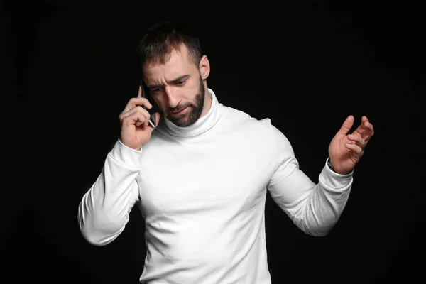 Portrait of young man talking by mobile phone on dark background — Stockfoto