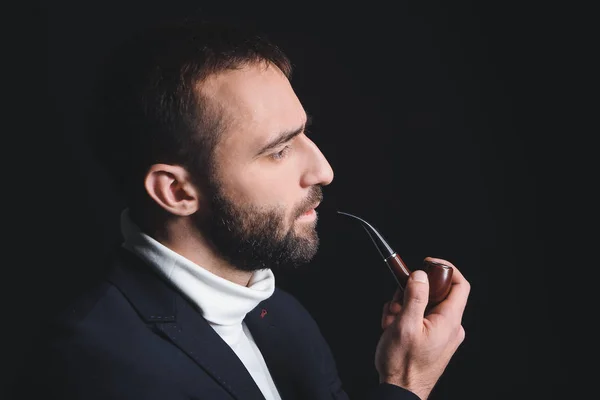 Portrait of stylish young man with smoking pipe on dark background — Stock Photo, Image