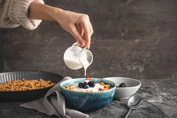 Woman preparing tasty granola with yogurt on grey background — Stock Photo, Image