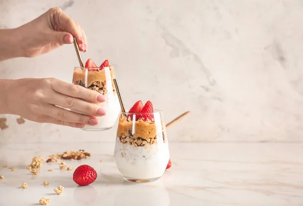 Female hands with glass of tasty granola and yogurt on white background — Stock Photo, Image