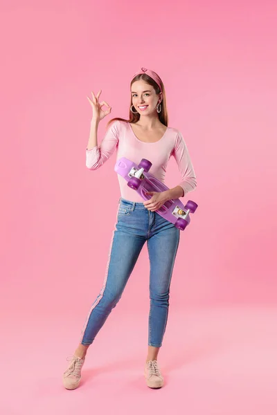 Stylish hipster girl with skateboard showing OK gesture on color background — ストック写真