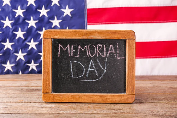 Chalkboard with text MEMORIAL DAY on table against USA flag — Stock Photo, Image