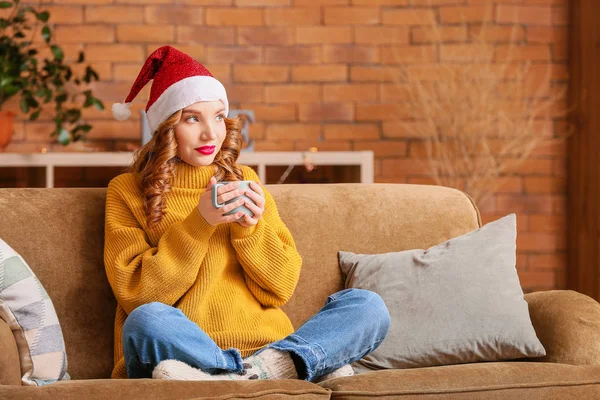 Junge Frau in Winterkleidung trinkt zu Hause heiße Schokolade auf dem Sofa — Stockfoto