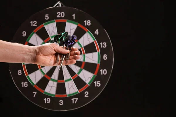 Férfi kéz darts és dartboard sötét háttér — Stock Fotó