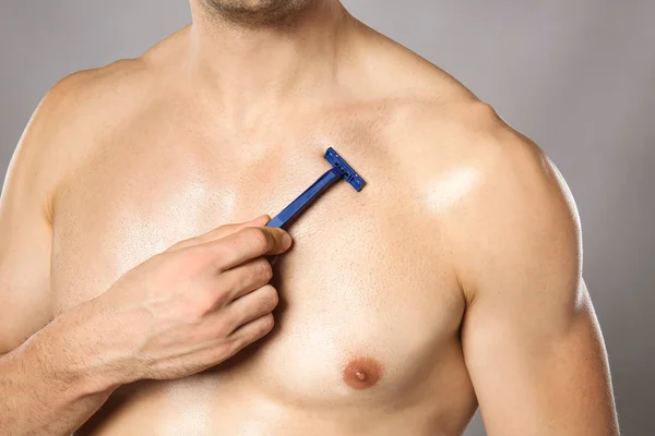 Handsome young man shaving his body on grey background, closeup — Stock Photo, Image