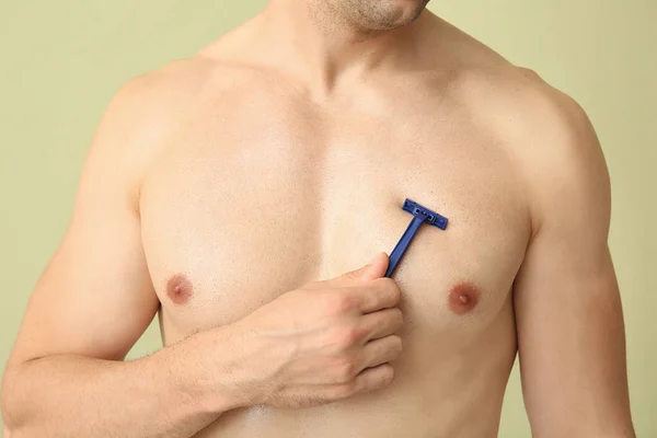 Hombre joven guapo afeitándose el cuerpo sobre fondo de color, primer plano — Foto de Stock