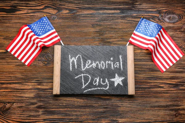 Chalkboard with text MEMORIAL DAY and USA flags on wooden background — Stock Photo, Image