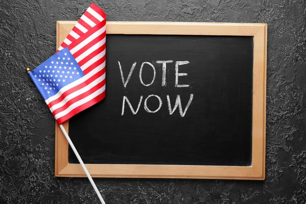 Chalkboard with text VOTE NOW and USA flag on dark background — Stock Photo, Image