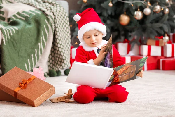 Söt liten pojke i tomte kostym och med bok hemma på julafton — Stockfoto