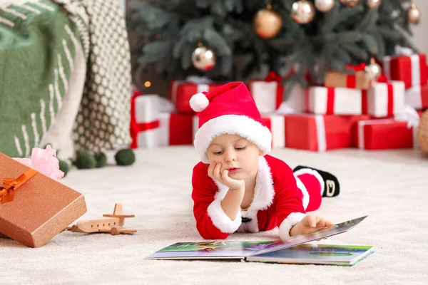 Cute little boy w stroju Mikołaja i z książki w domu na Wigilię — Zdjęcie stockowe