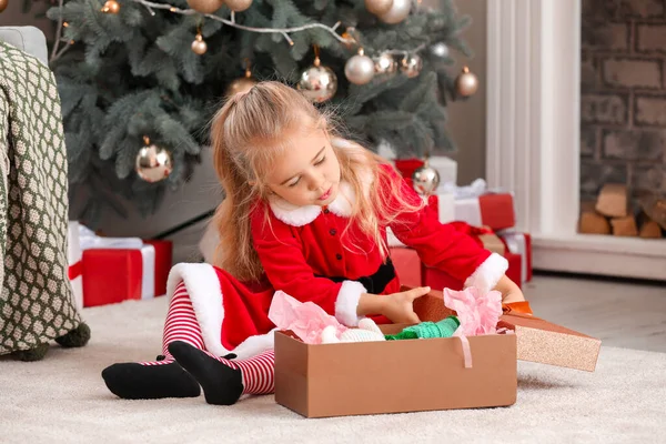 Süßes kleines Mädchen im Weihnachtsmannkostüm und mit Weihnachtsgeschenk zu Hause — Stockfoto