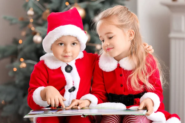 Cute little children in Santa costumes and with book at home on Christmas eve — Stock Photo, Image