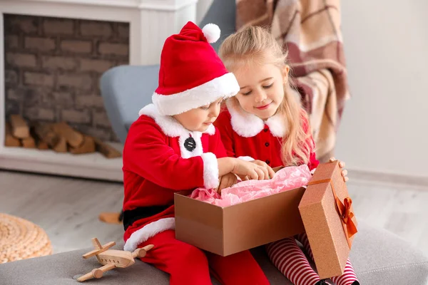 Lindos niños pequeños en trajes de Santa y con regalo de Navidad en casa — Foto de Stock