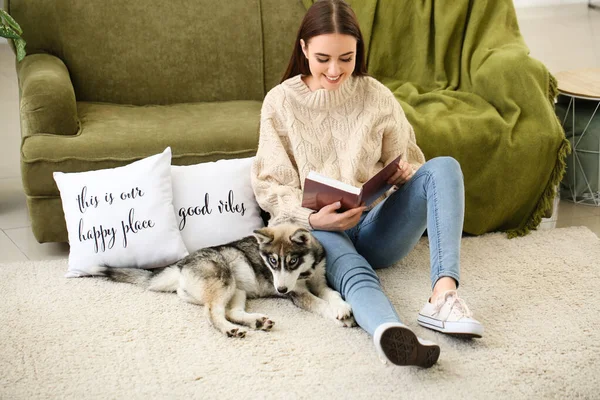 Giovane donna con divertente husky cucciolo lettura libro a casa — Foto Stock