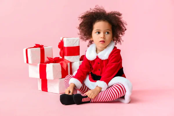 Little African-American girl in Santa costume and with gift boxes on color background — Stock Photo, Image