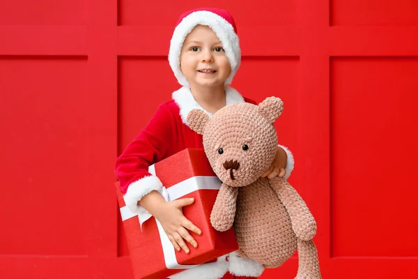 Mignon petit garçon en costume de Père Noël, avec cadeau de Noël et ours jouet sur fond de couleur — Photo